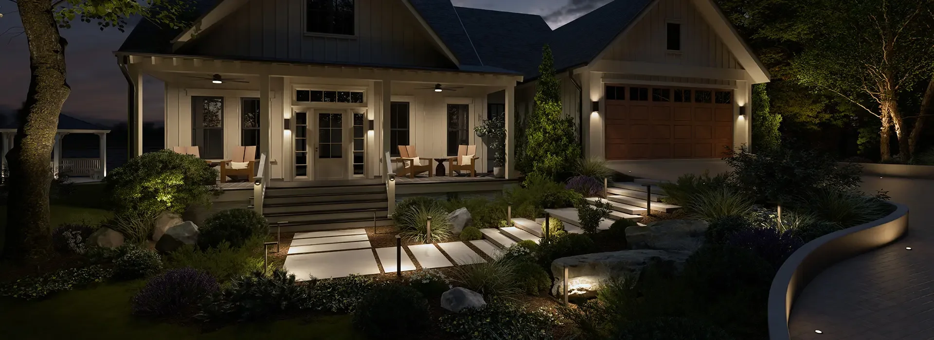 A house exterior at night with porch lights, a front porch with chairs and plants, stairs leading to a landscaped garden, and a garage, illuminated by outdoor lighting.