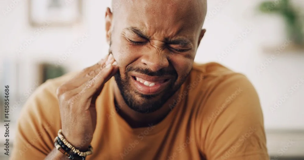 A man experiencing pain or discomfort, holding his jaw or cheek with a pained expression.