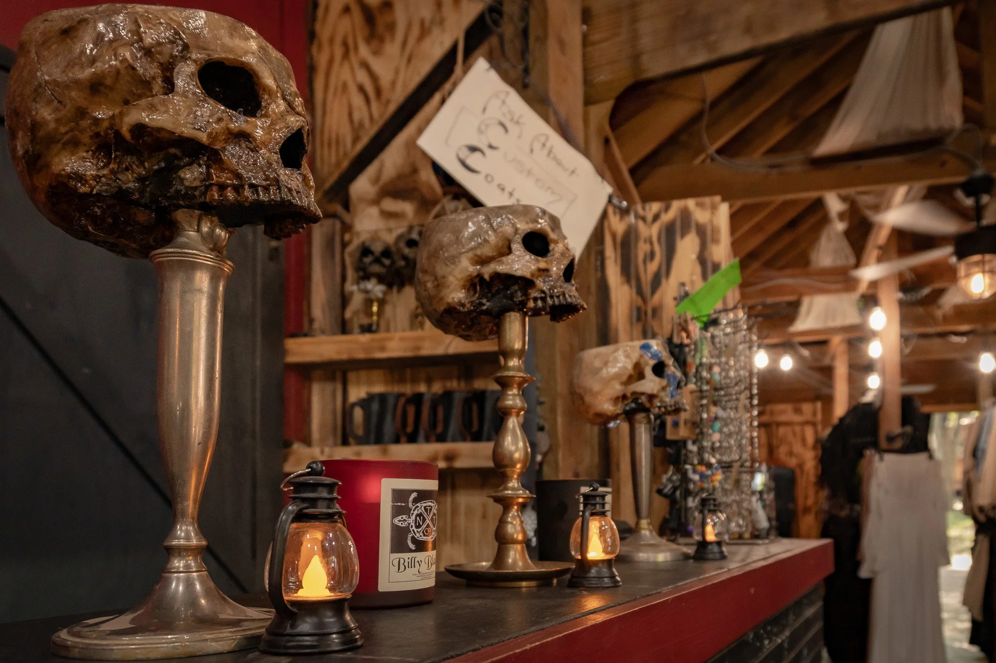 Display of three metallic skull sculptures on stands, candles, and jewelry against a rustic wooden background.