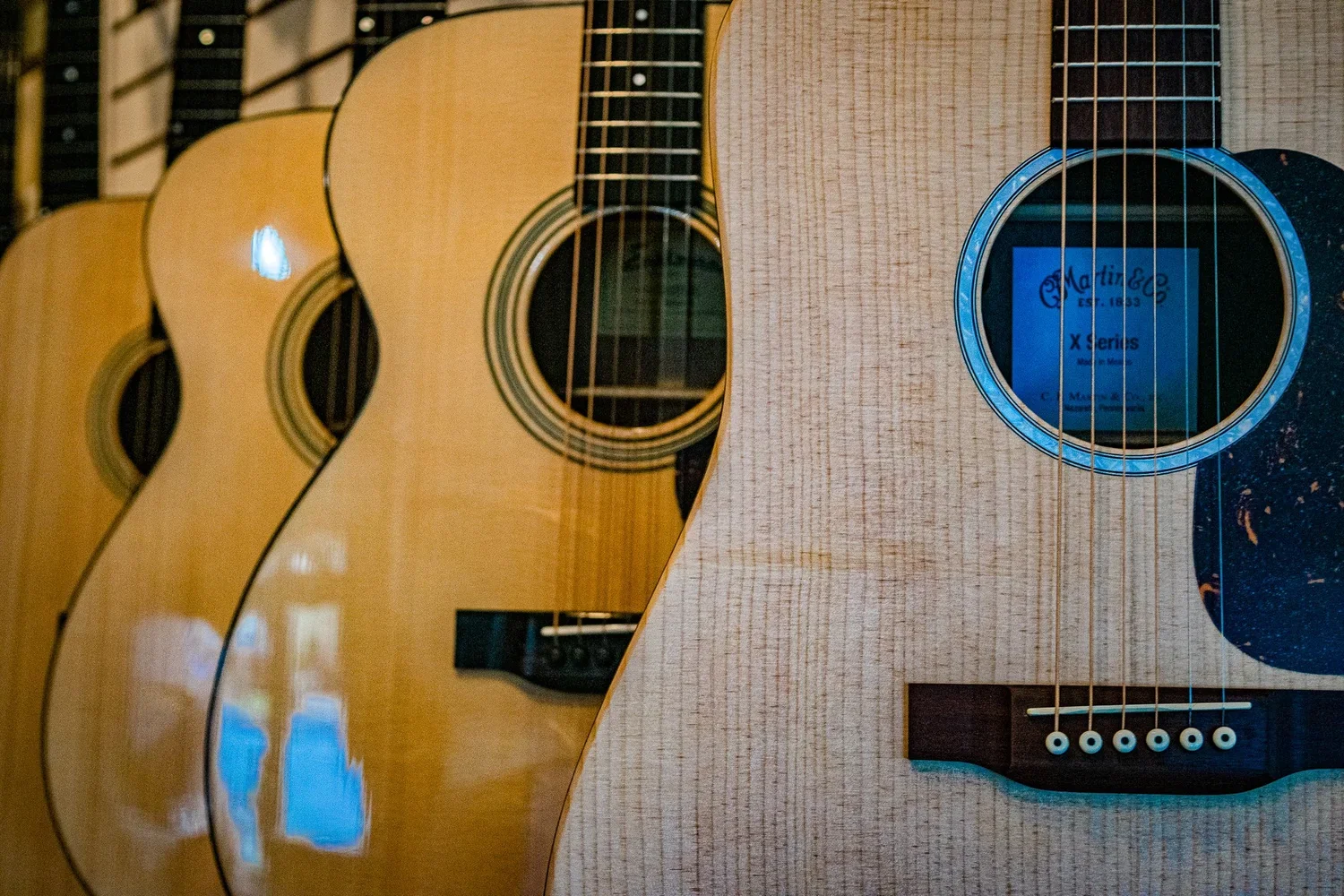 Several acoustic guitars hanging on a wall, with the strings and soundholes visible.
