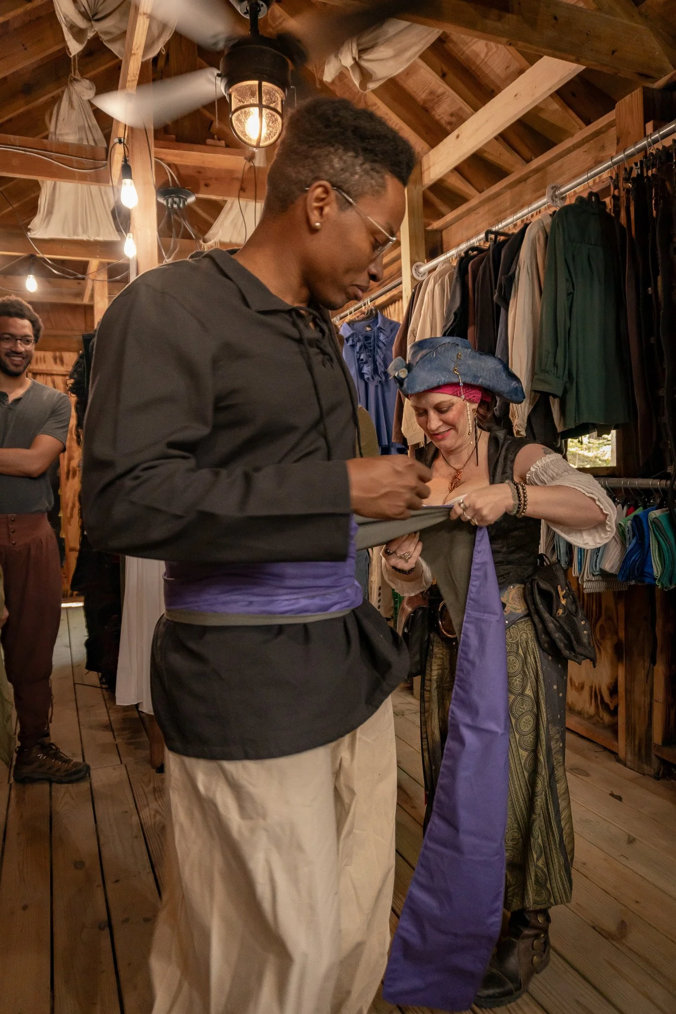 People inside a rustic boutique or costume shop, one person dressed as a pirate, others looking at costumes or clothing.