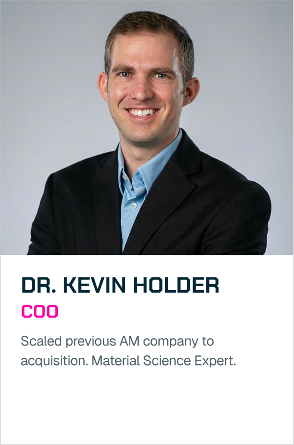 A professional headshot of a smiling man in a black suit jacket and light blue dress shirt against a gray background.