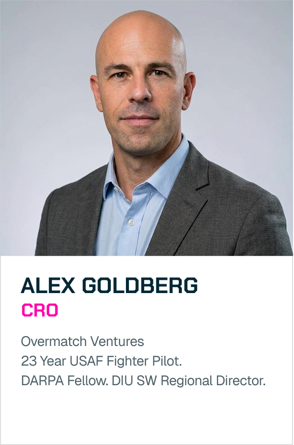 A professional headshot of a bald man in a gray suit and light blue shirt against a plain gray background.