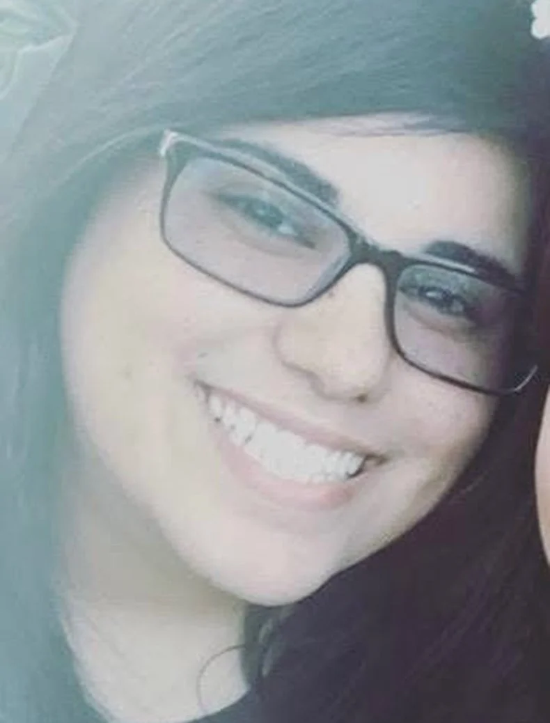 Close-up of a woman with long dark hair, glasses, and a bright smile showing her teeth.