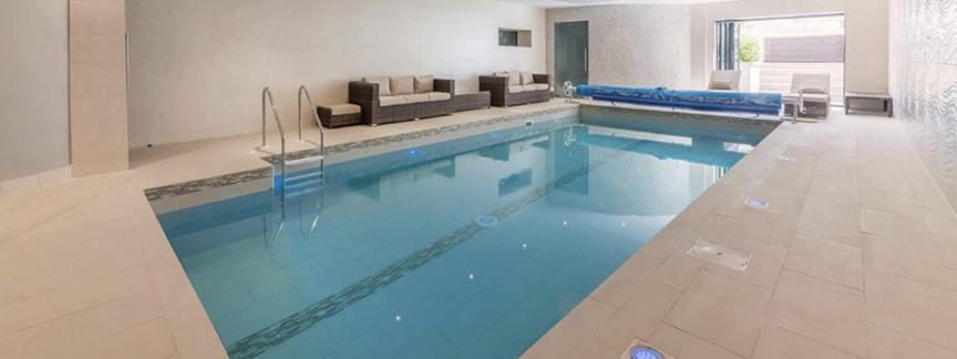 Indoor swimming pool area with lounge chairs and a closed pool cover.