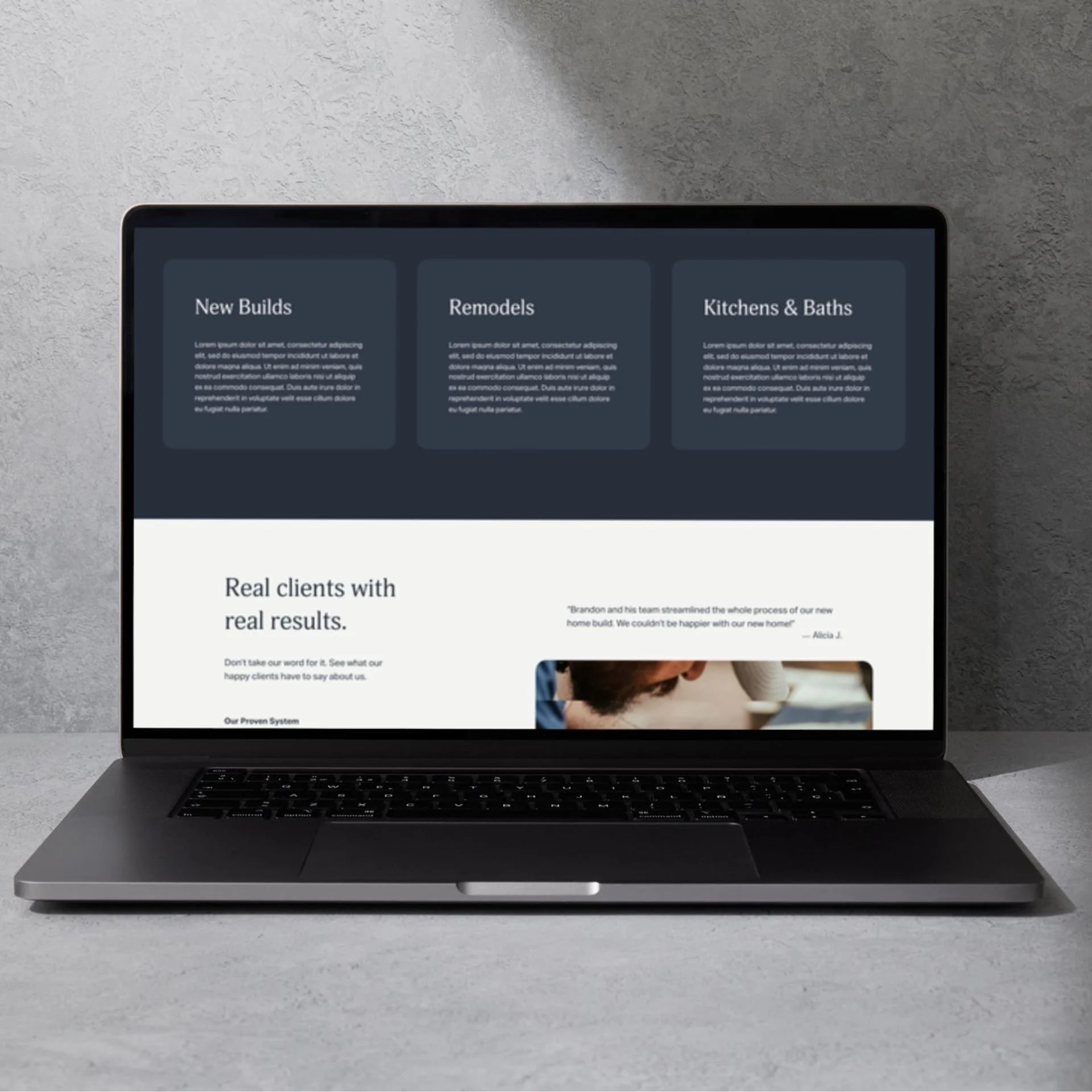 Open laptop on a concrete surface displaying a website with sections on New Builds, Remodels, and Kitchens & Baths.