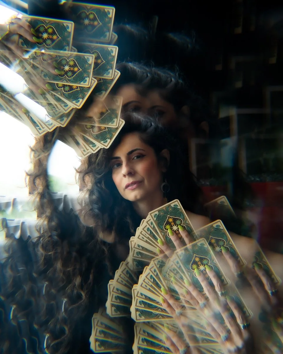 A woman with curly hair holding playing cards displayed in a mirror