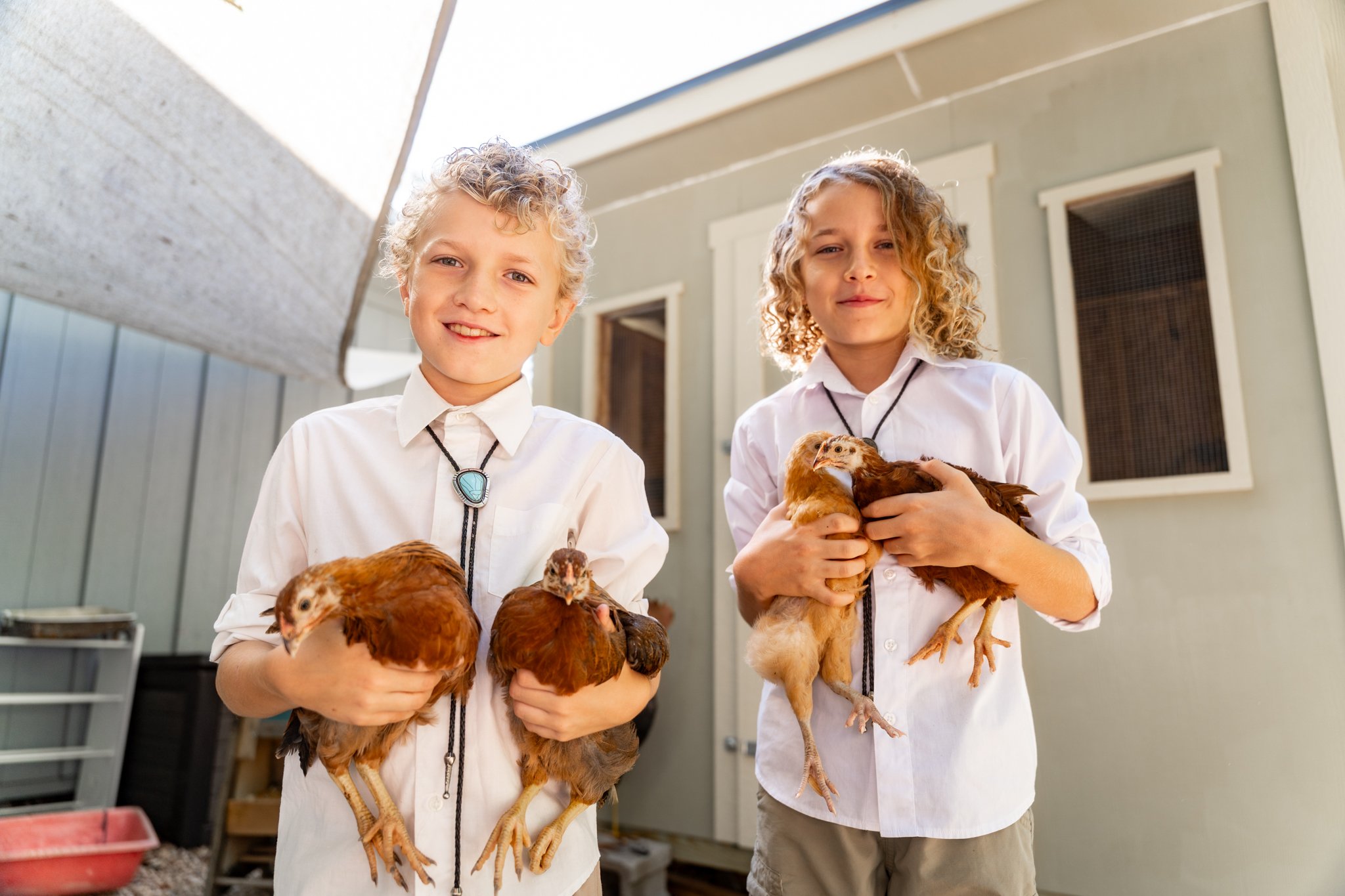 Two children holding chickens outdoors, smiling at the camera.