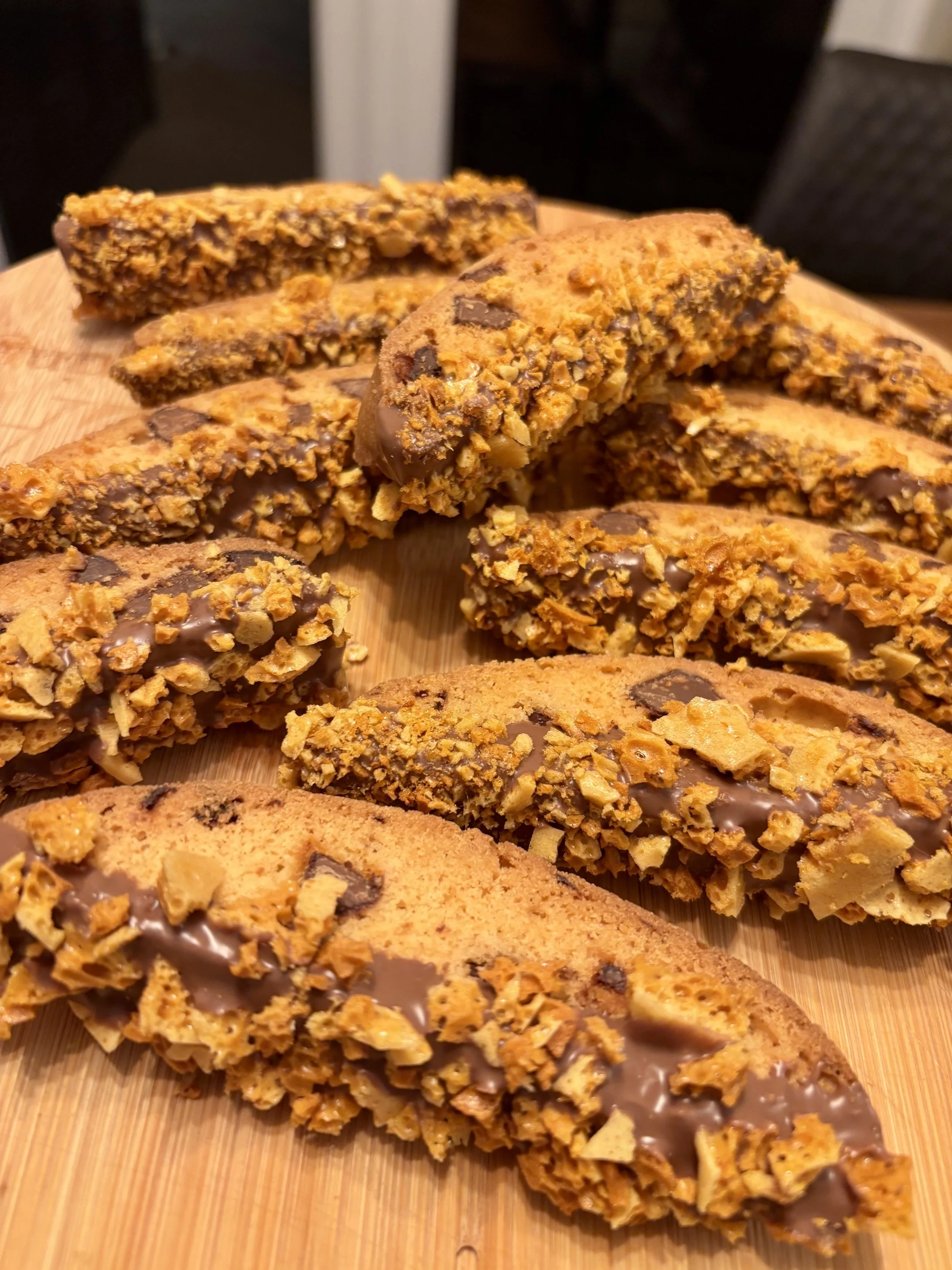A close-up of several biscotti cookies with chopped nuts and chocolate pieces on a wooden surface.