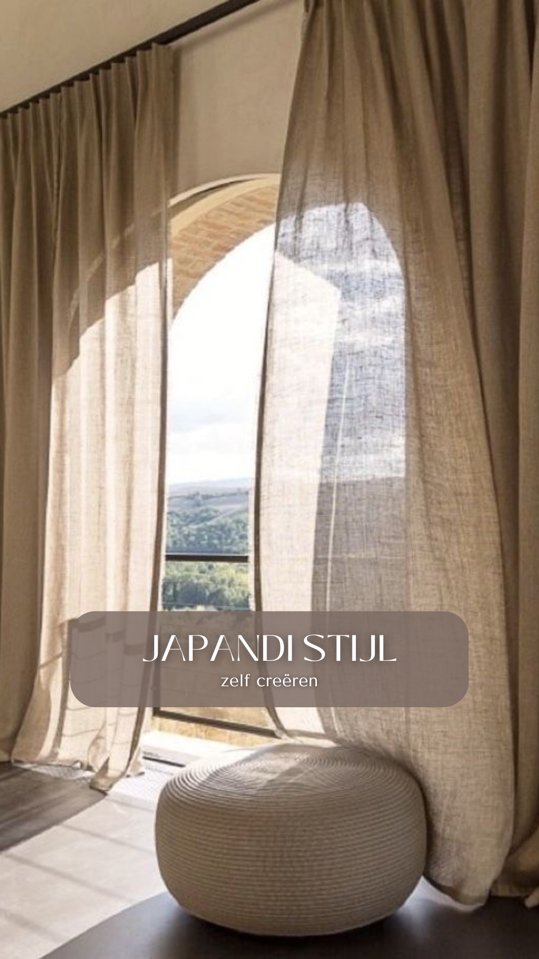 Curtains partially open, revealing an arched window with scenic landscape view outside and a round textured beige ottoman in the foreground.