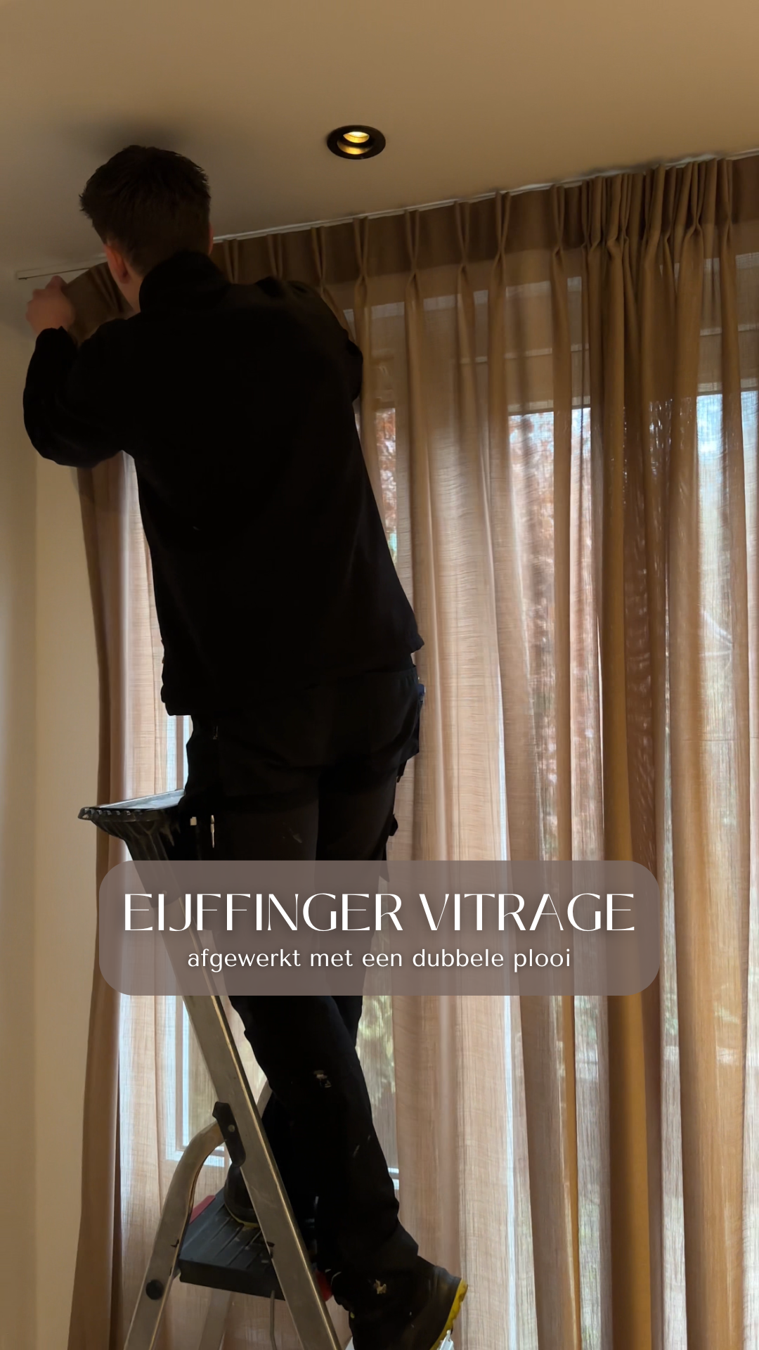 A person standing on a step ladder working on a ceiling light fixture near beige curtains.