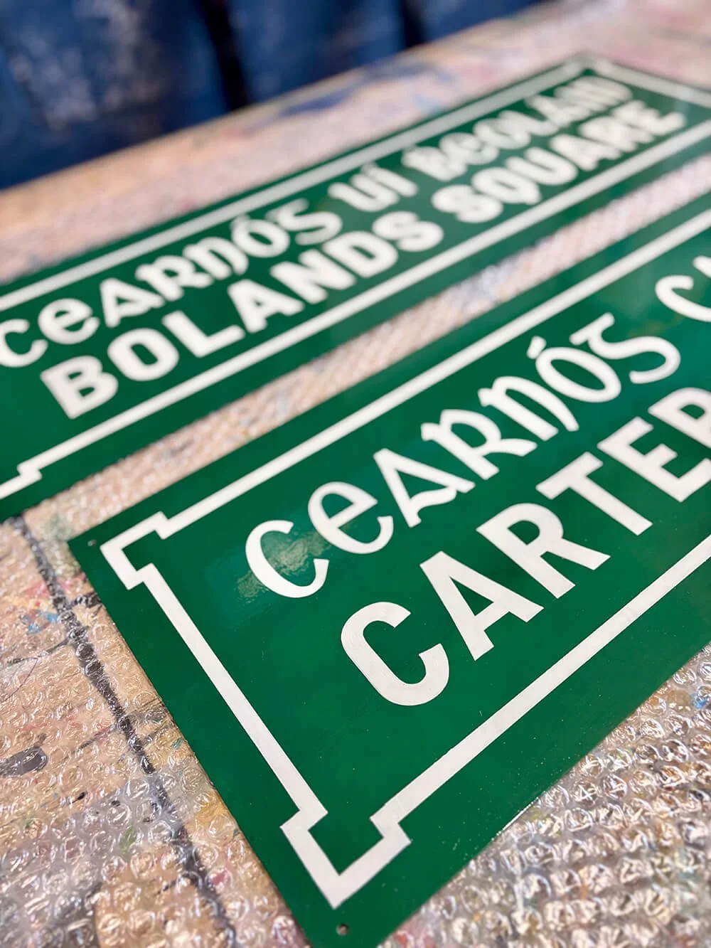 Green traditional street sign swith white text.  The sign is lying on a bubble wrap surface.