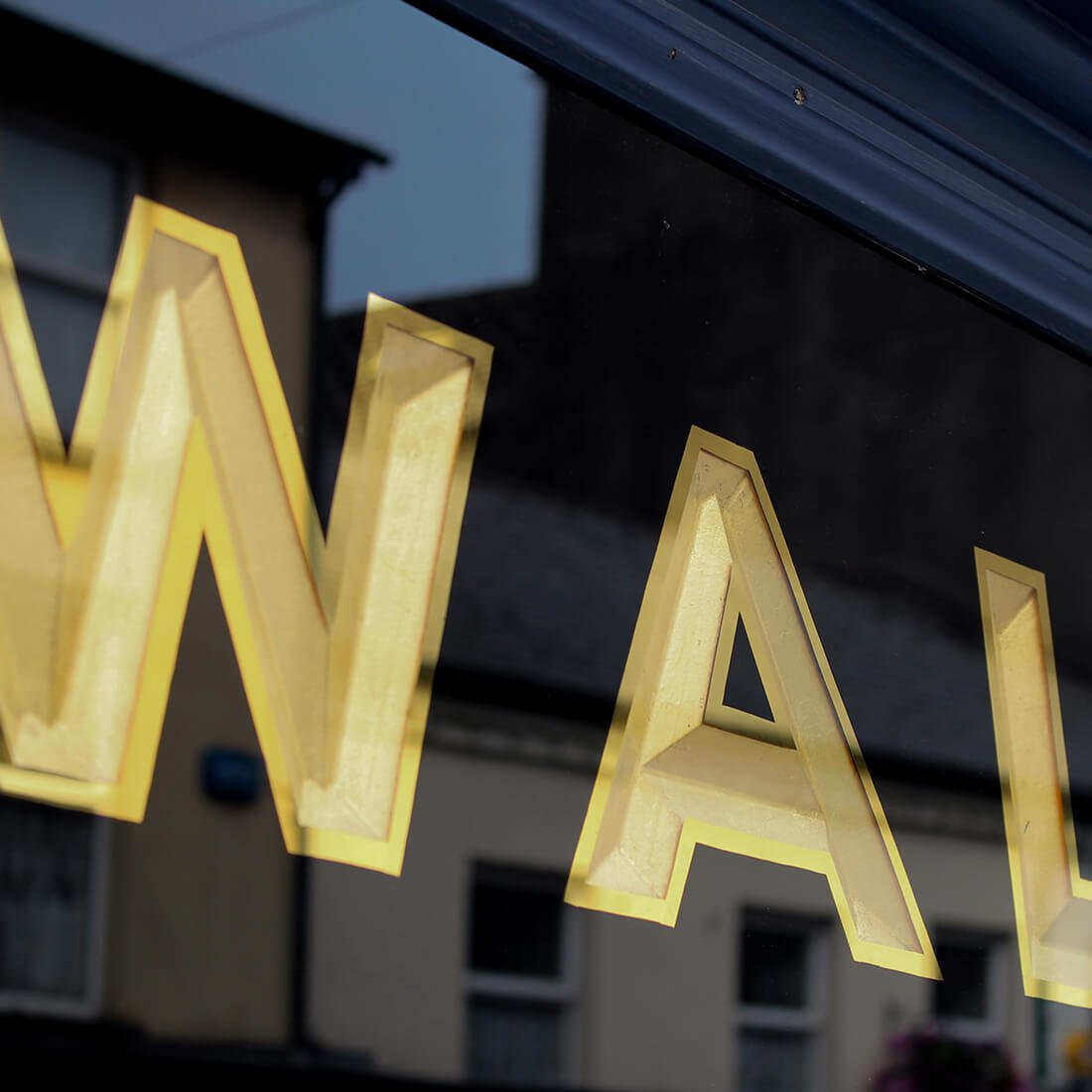 Close-up of illuminated yellow letter sign spelling 'WALL' reflected in window glass.