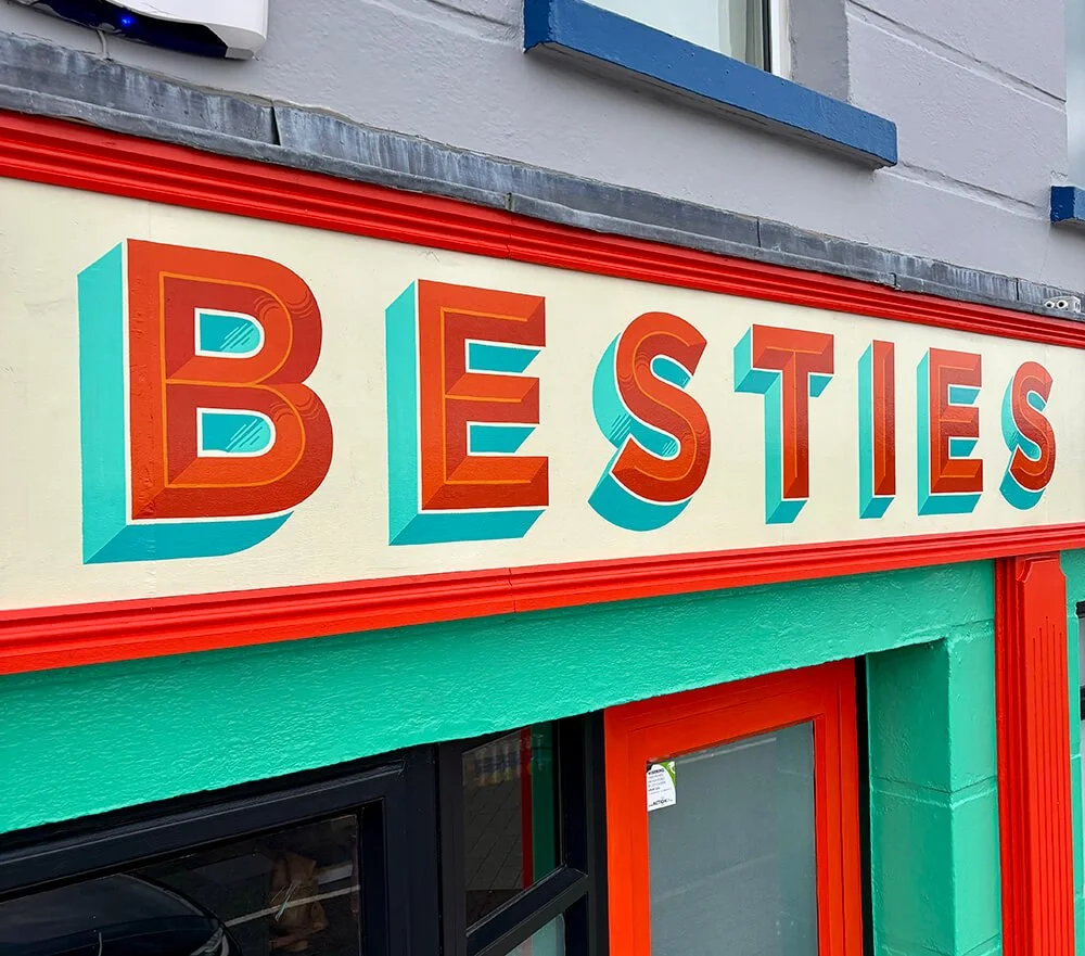 Colorful storefront sign reading 'BESTIES' with bold red and turquoise 3D letters.