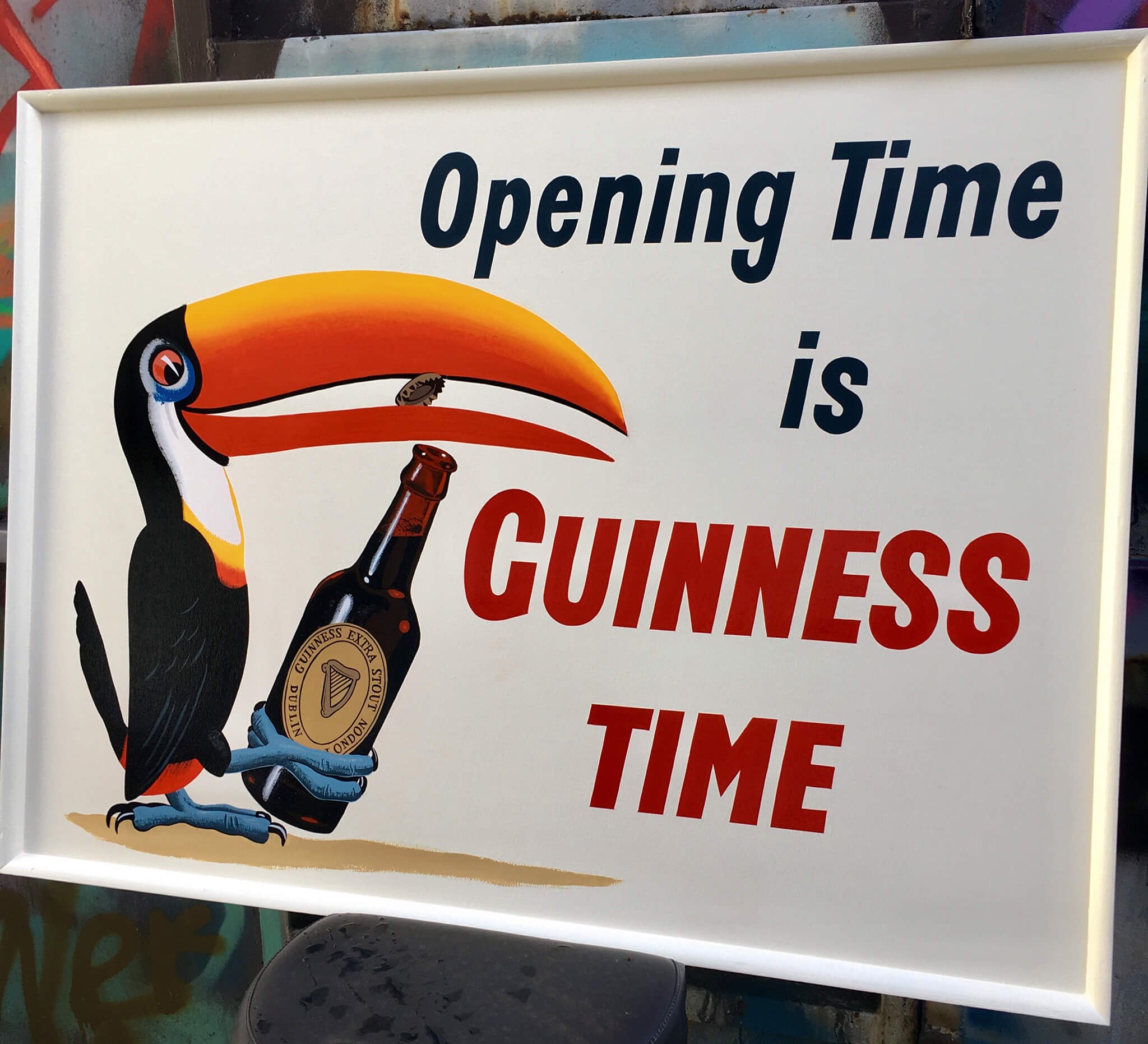 Sign with a toucan holding a Guinness beer bottle, advertising the opening time with the text 'Opening Time is Guinness Time'.