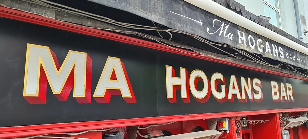 Exterior sign of Hogans Bar with large yellow and red lettering on a black background, and a red border.