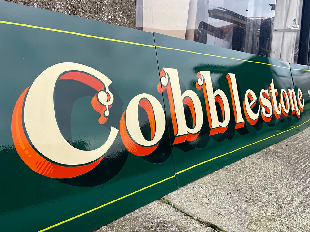 Colored sign with the text 'Cobblerstone' in large stylized letters, placed on a concrete ground.