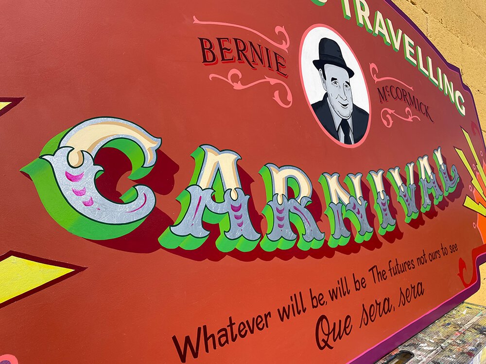 A colorful sign with the words "CARNIVAL" in large decorative letters, a black-and-white portrait of a man wearing a hat with the name "BERNIE McCORMICK" above it, and a quote that says "Whatever will be, will be. The futures not ours to see."