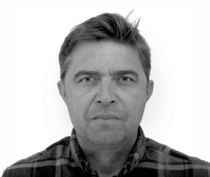 Black and white portrait of a man with short, combed hair wearing a plaid shirt, looking directly at the camera