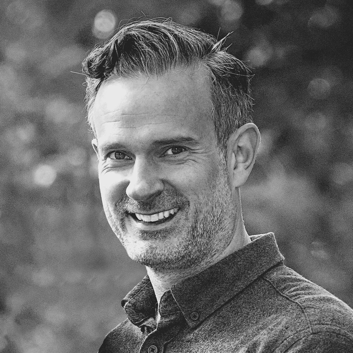 Black and white portrait of a smiling man with short hair and a beard, wearing a collared shirt.