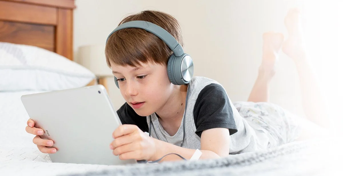 Adolescent male wearing headphones and using a tablet to engage in developmental skills supporting games and apps.