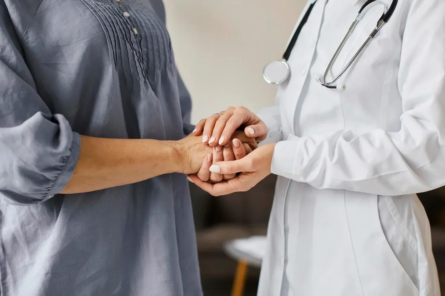 Healthcare professional in a white coat with a stethoscope holding a patient's hand.