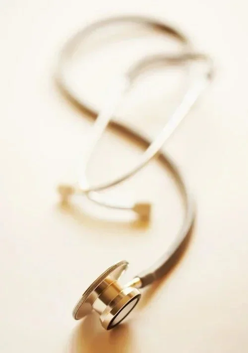 A gold-colored stethoscope with black tubing lying on a white surface.