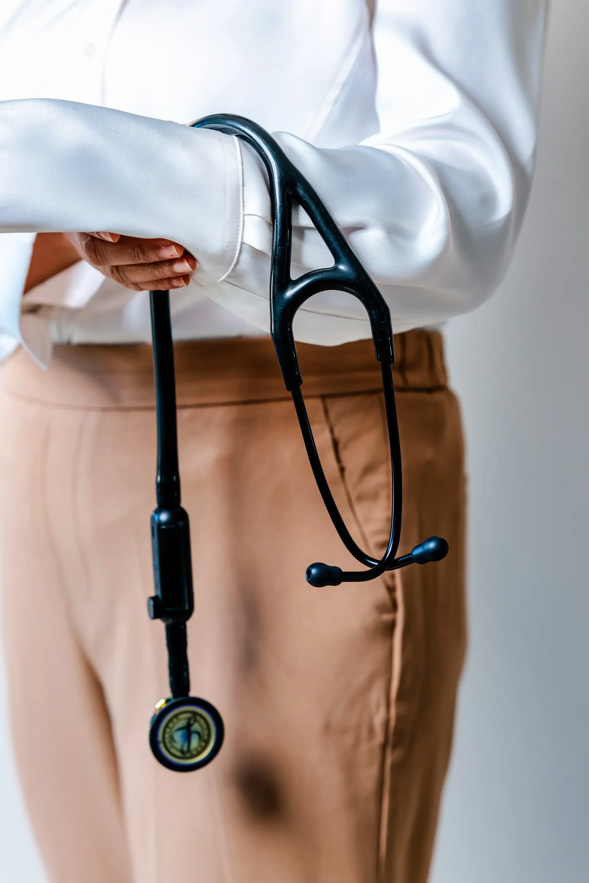 A person in beige pants and a white shirt holding a stethoscope.