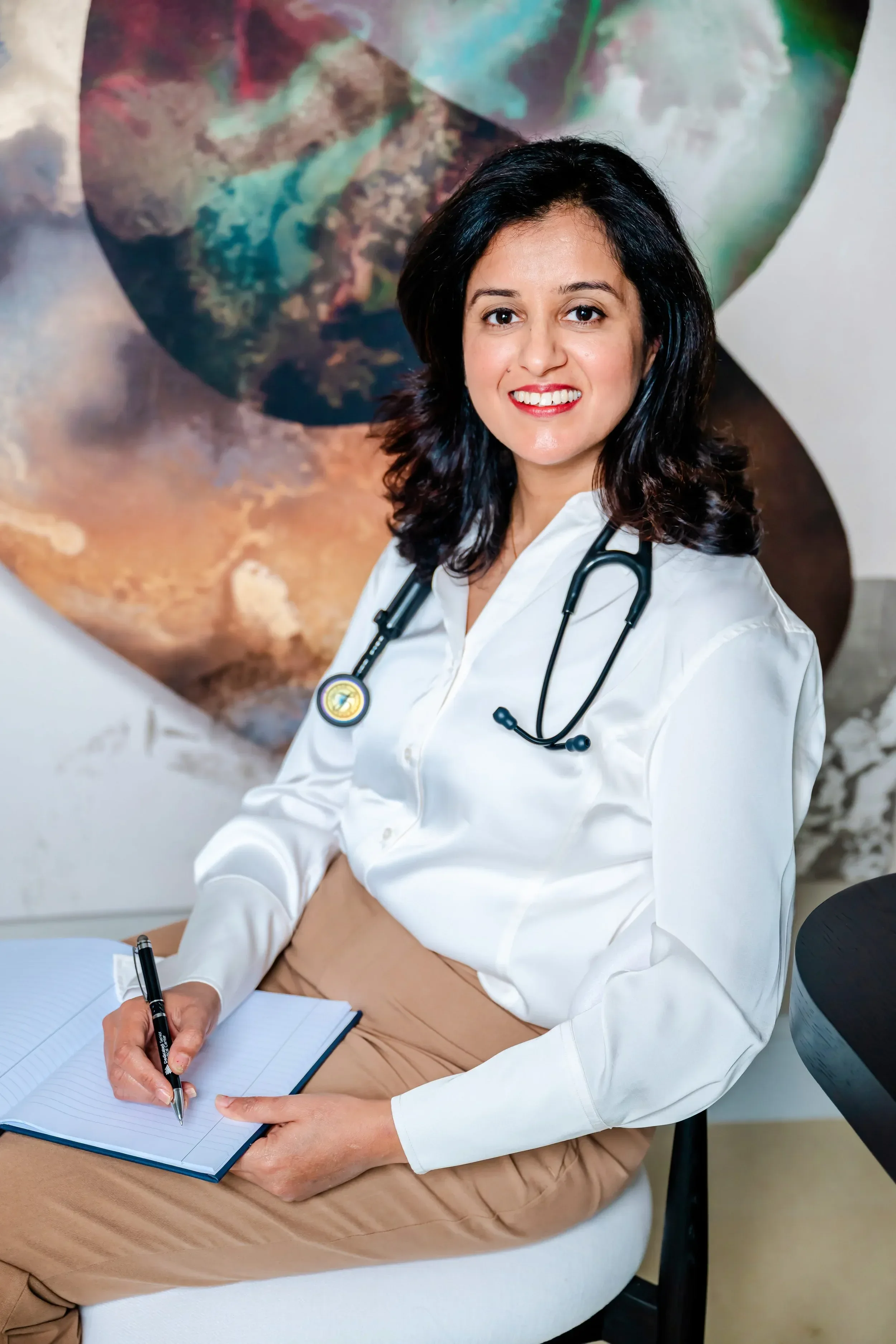 Dr. Rachita Bansal smiling and looking at the camera. In the background, there is a large colorful abstract painting.