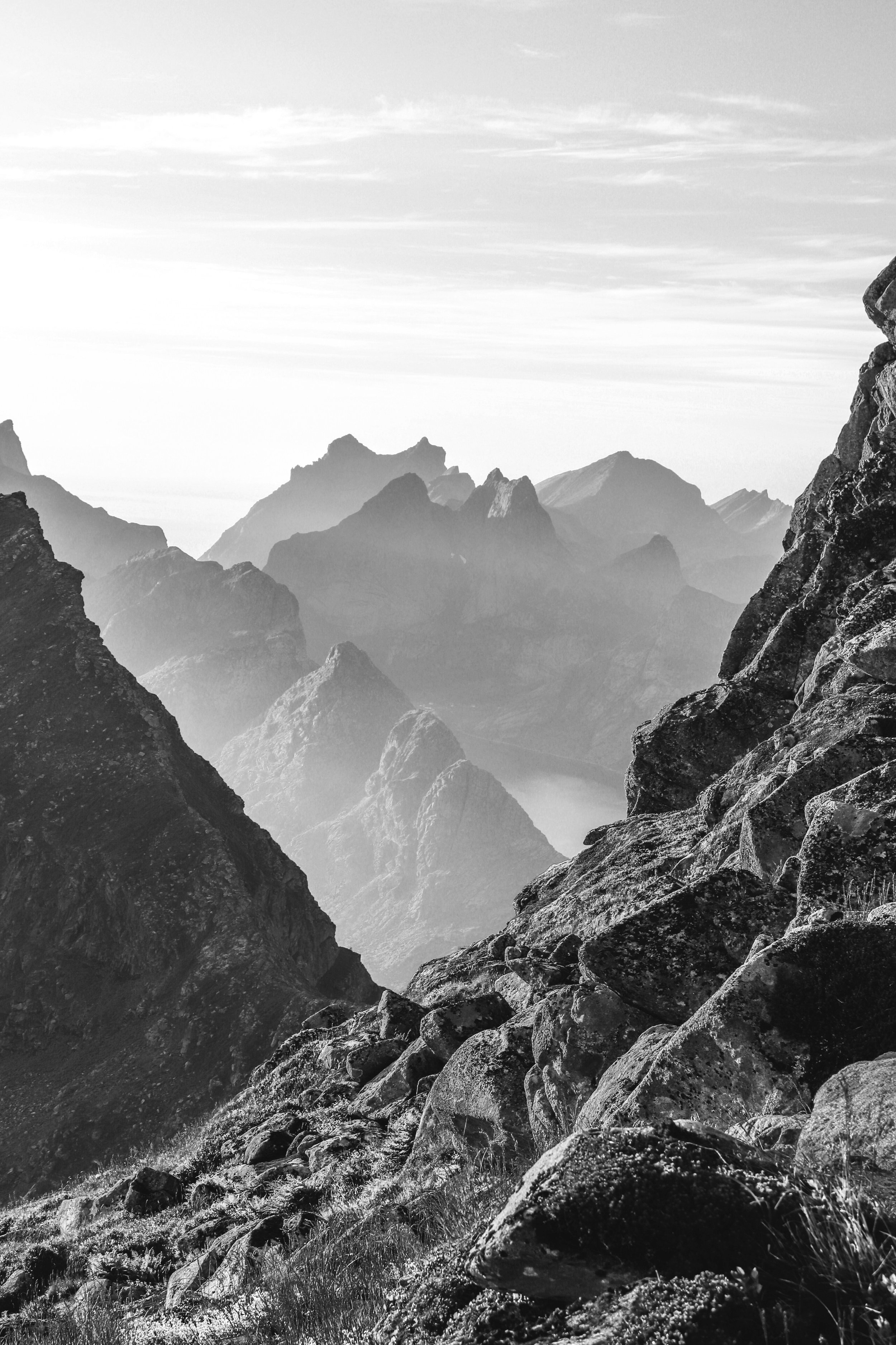 Black and white photo of rugged mountain range with steep rocky slopes and distant peaks under a cloudy sky.