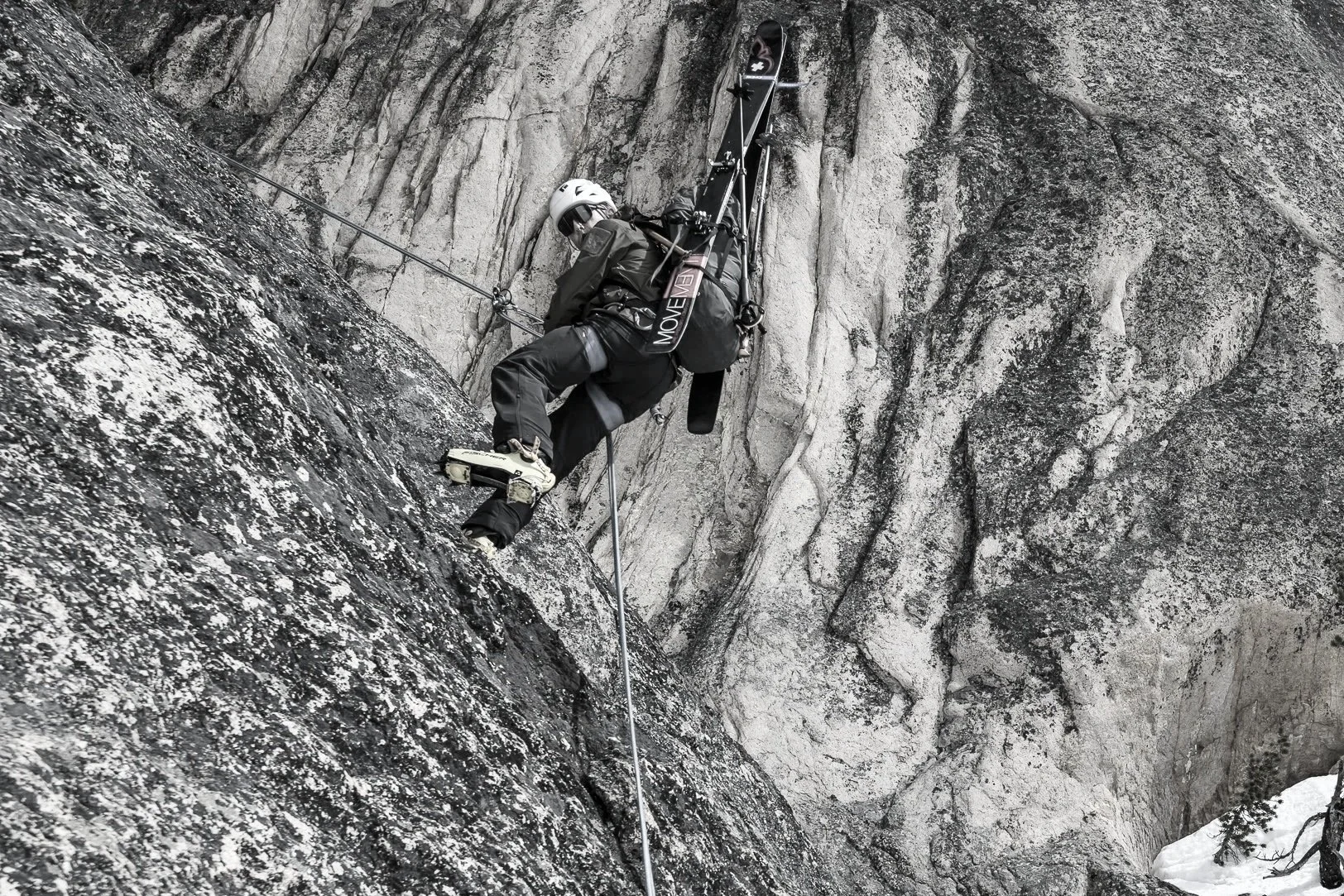 A person in climbing gear ascending a steep rock face, with a helmet, harness, and carabiners, surrounded by gray and black textured rock.