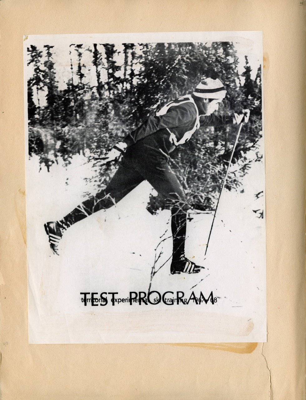 A person cross-country skiing on a snowy forest trail, dressed in winter sports gear including a headband and ski boots, holding ski poles.