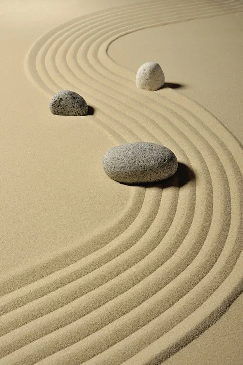 Three stones placed on raked sand in a Zen garden, creating concentric curved lines.