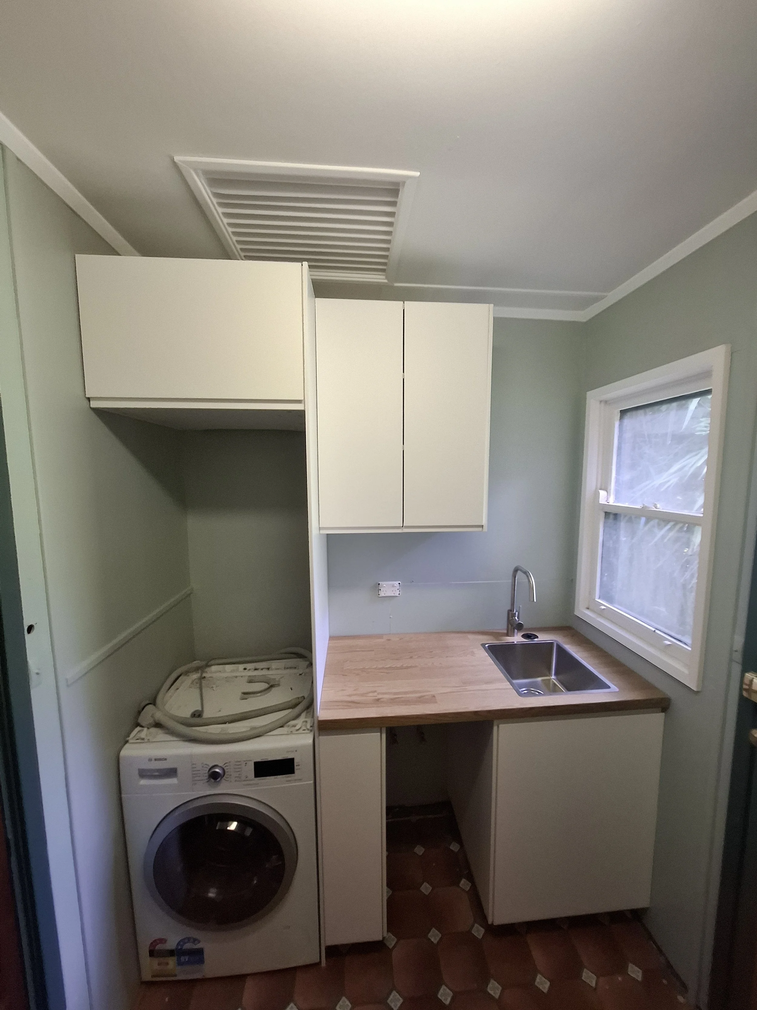 Small laundry area with washing machine, countertop, and cabinet, next to a window with a view outside.
