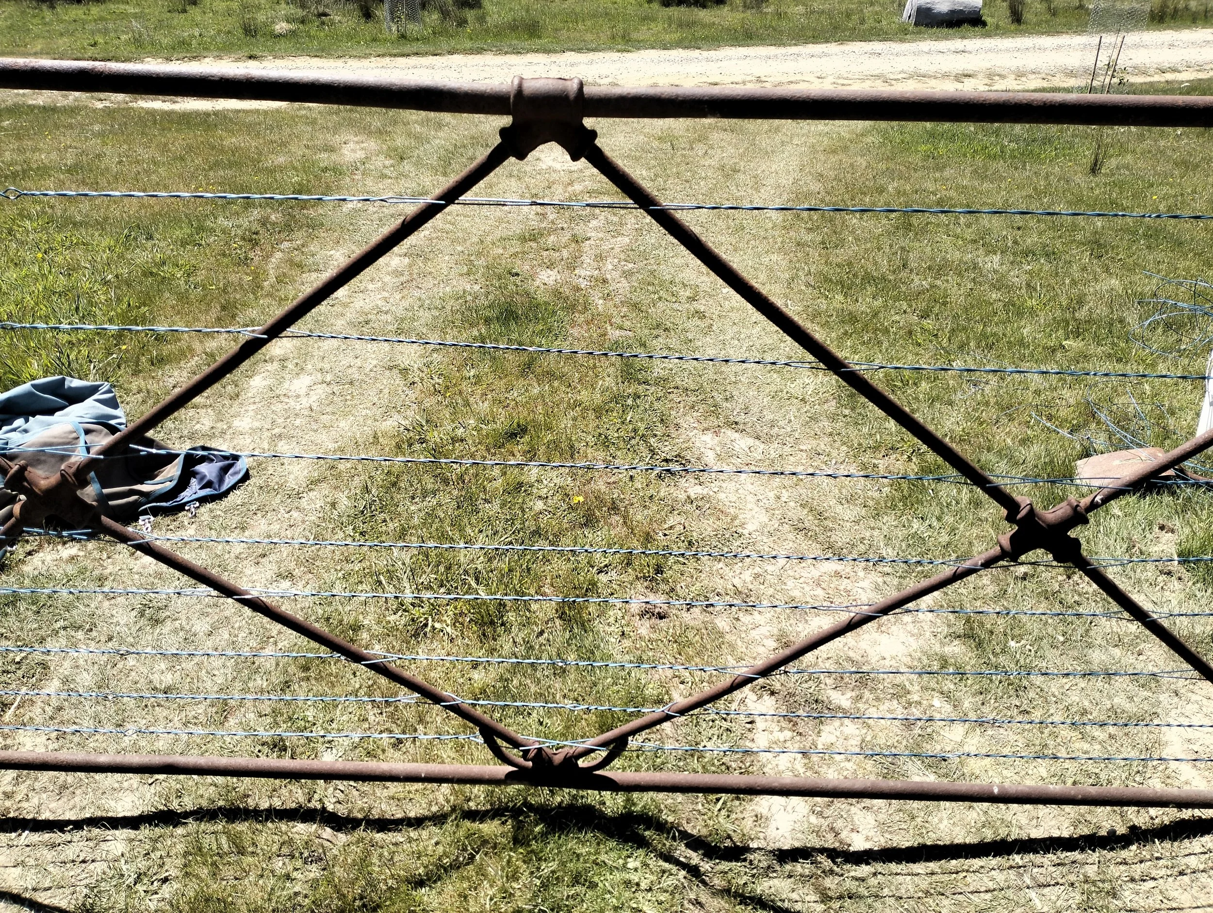 Rusty metal gate with barbed wire on a grassy area with some clothing on the ground to the left.