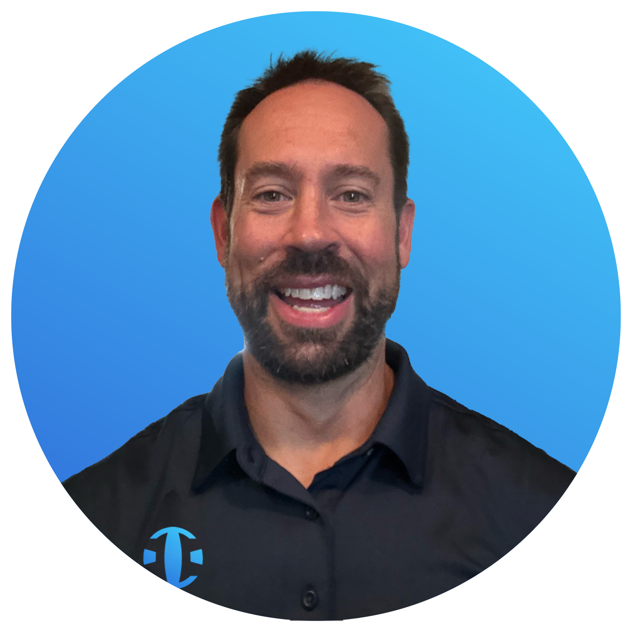 A man with a beard and mustache smiling, wearing a black collared shirt with a logo on the left side, against a blue background with a circular border.