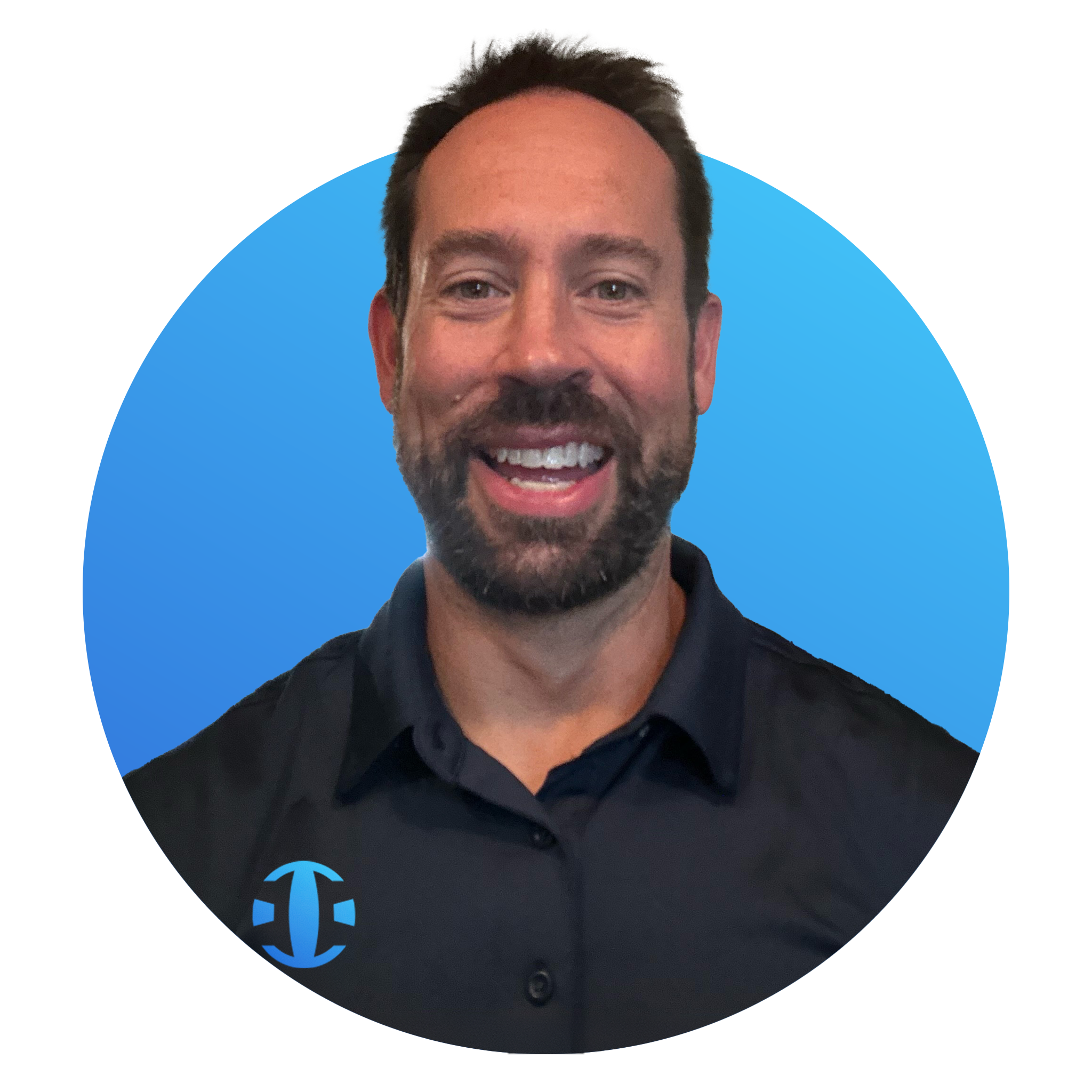 A man with dark hair and a beard, smiling, wearing a dark collared shirt with a logo on the chest, standing in front of a blue background.