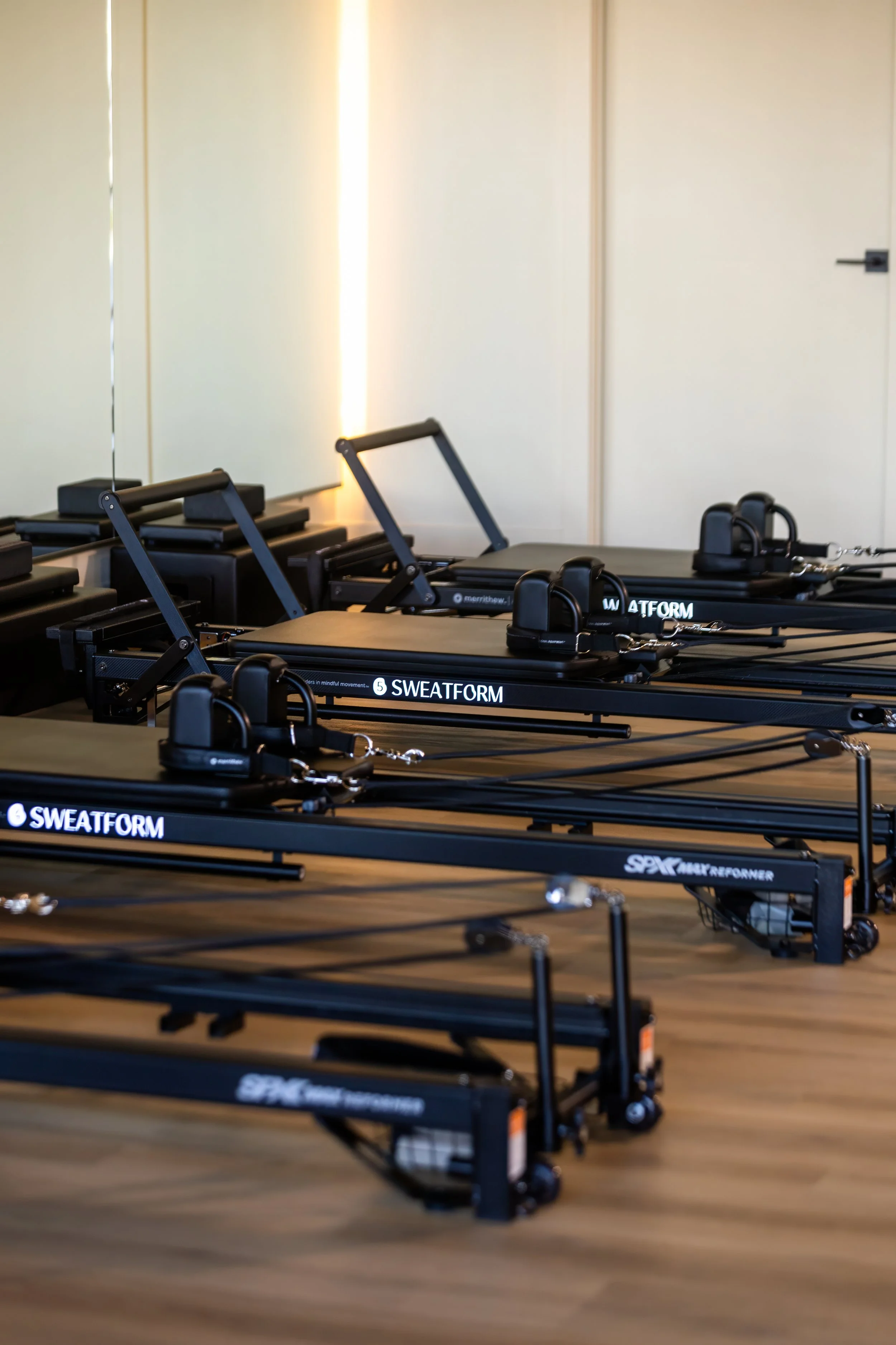 Pilates reformer machines in a fitness studio with hardwood floors and a mirror wall.