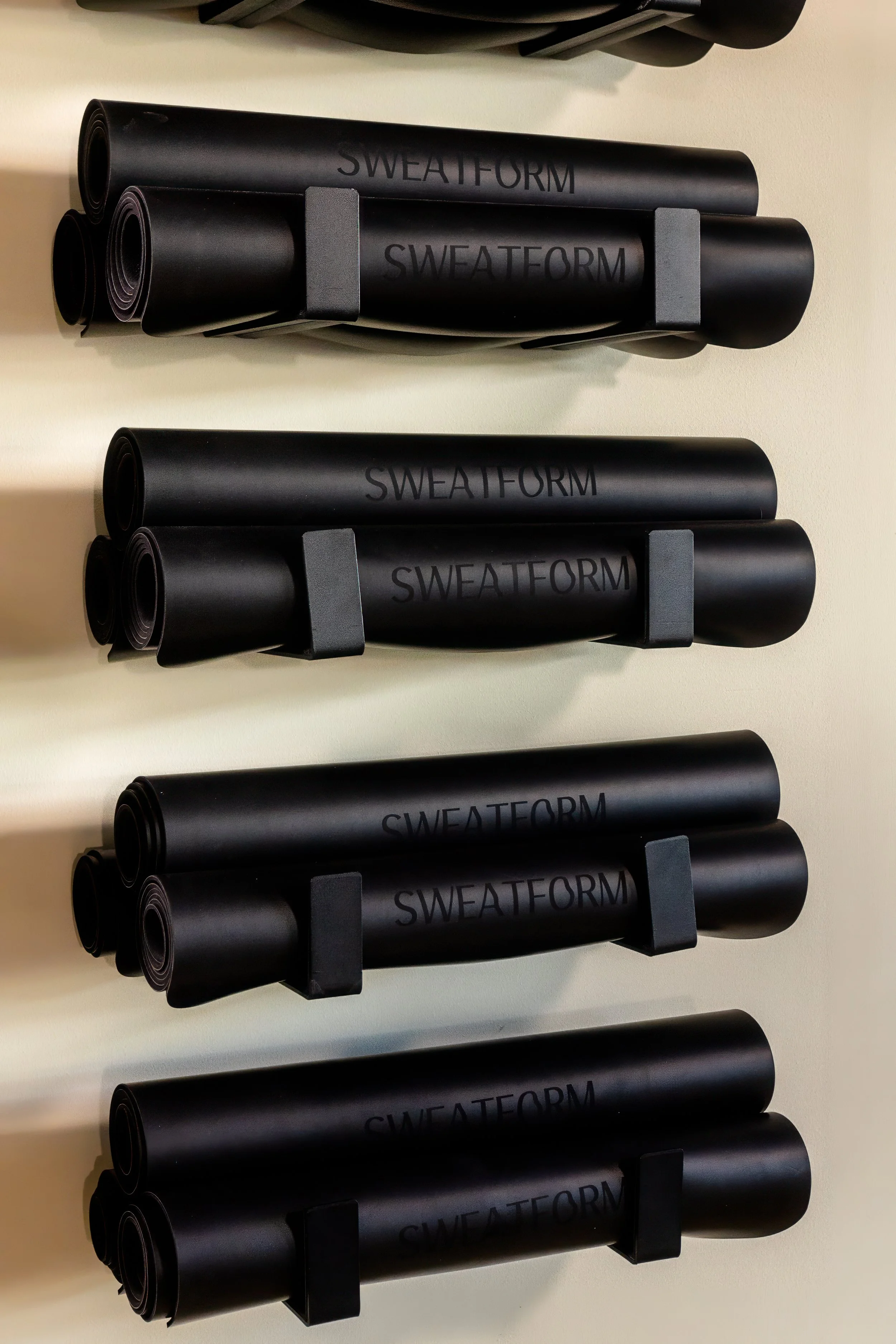 Four sections of rolled black fitness mats with 'SWEATFORM' branding, mounted on a beige wall with black supports.