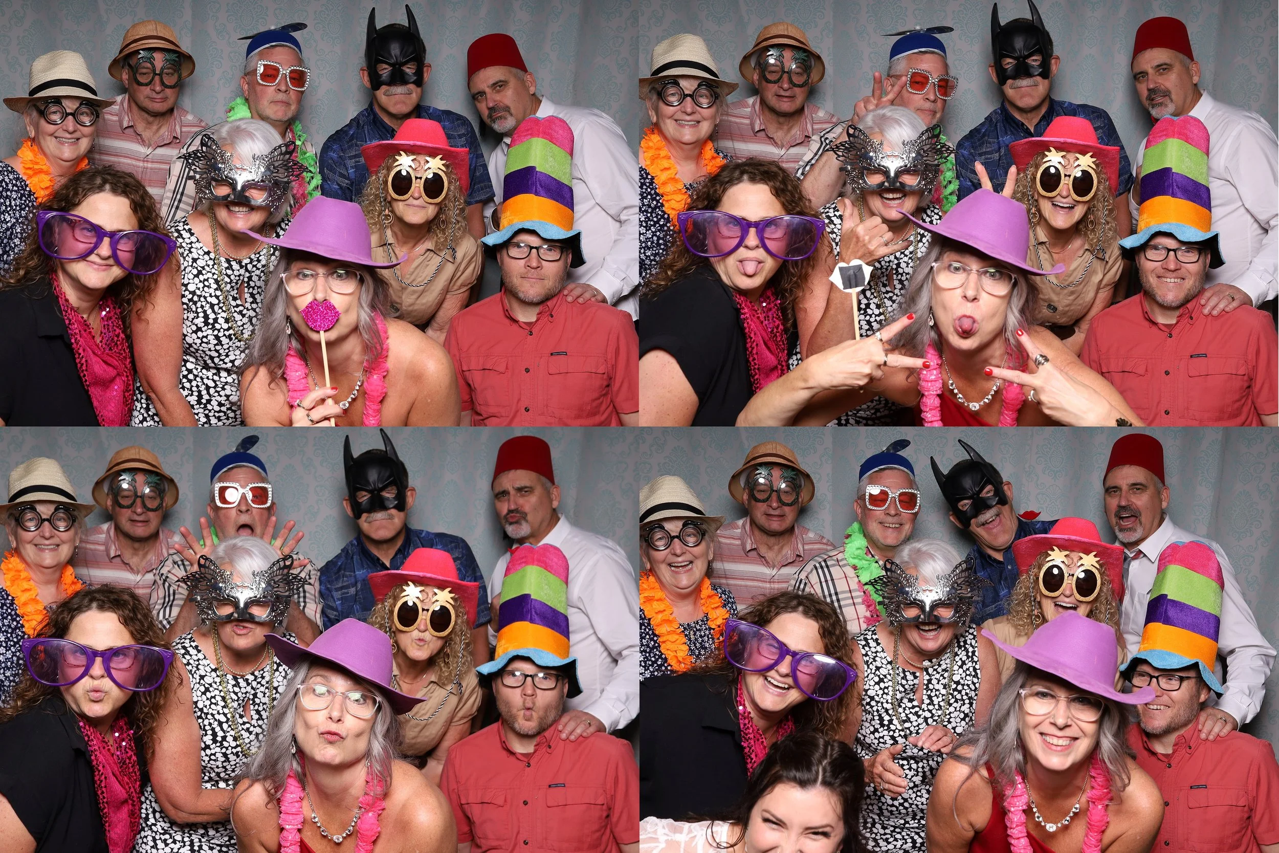 Group of people with colorful costumes, masks, and props in a photo booth. They are wearing glasses, hats, and leis, making funny faces and posing with peace signs.