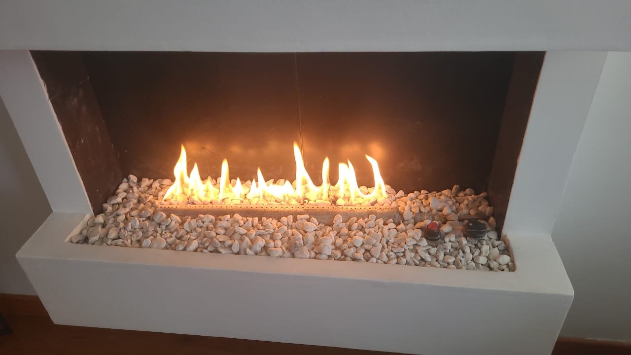 Chimenea moderna con fuego encendido sobre piedras decorativas blancas.