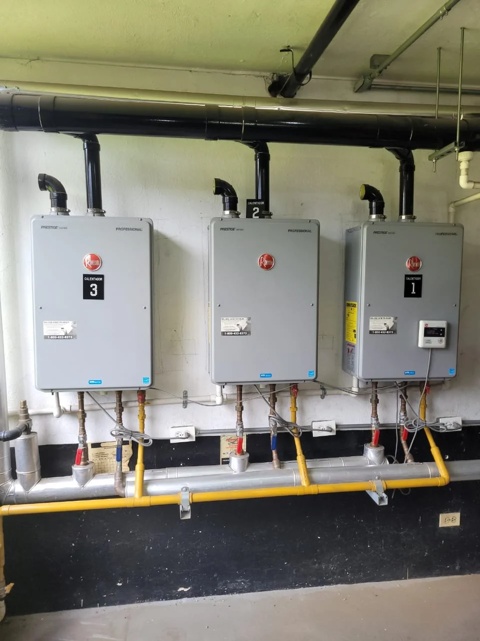 Tres calderas de agua con conexiones de tuberías en una sala de mantenimiento.