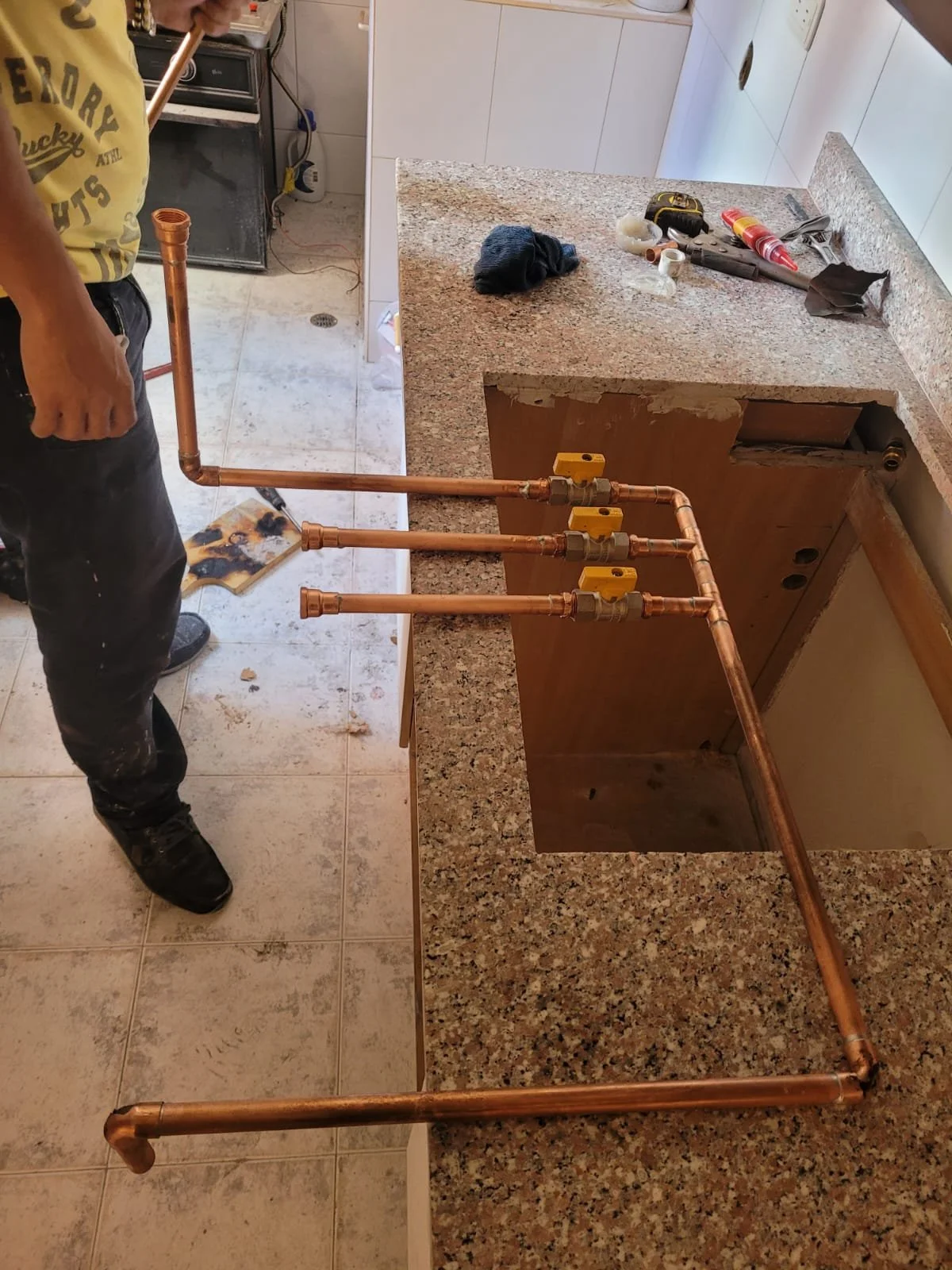 Trabajador instalando tuberías de cobre en una cocina. Herramientas y materiales de plomería sobre la encimera.