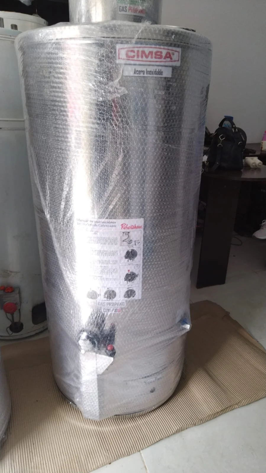 Calentador de agua de acero inoxidable cubierto con burbuja plástica para protección.