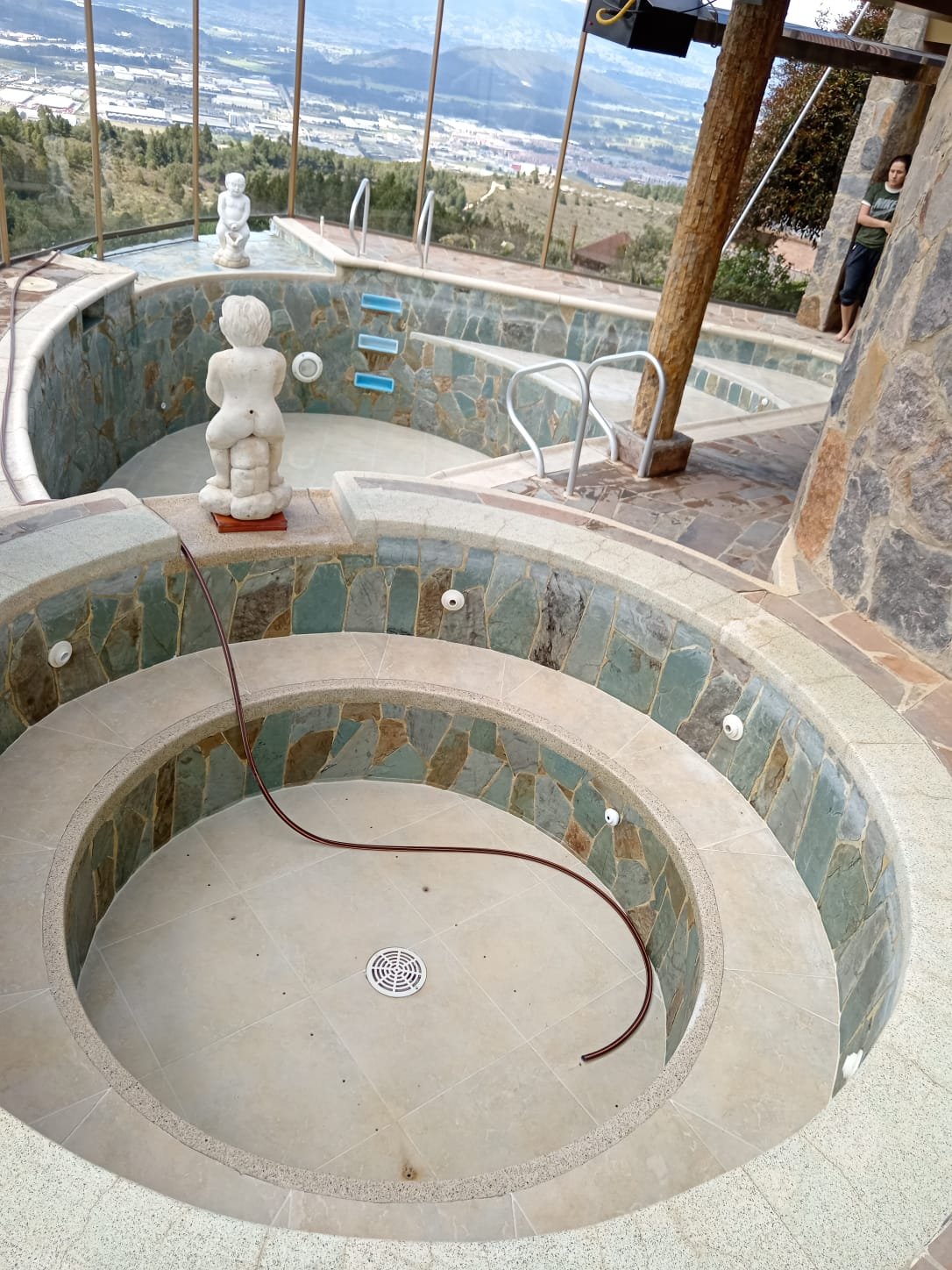 Piscina de jacuzzi sin agua con adornos de estatuas y vistas de la ciudad en el fondo.