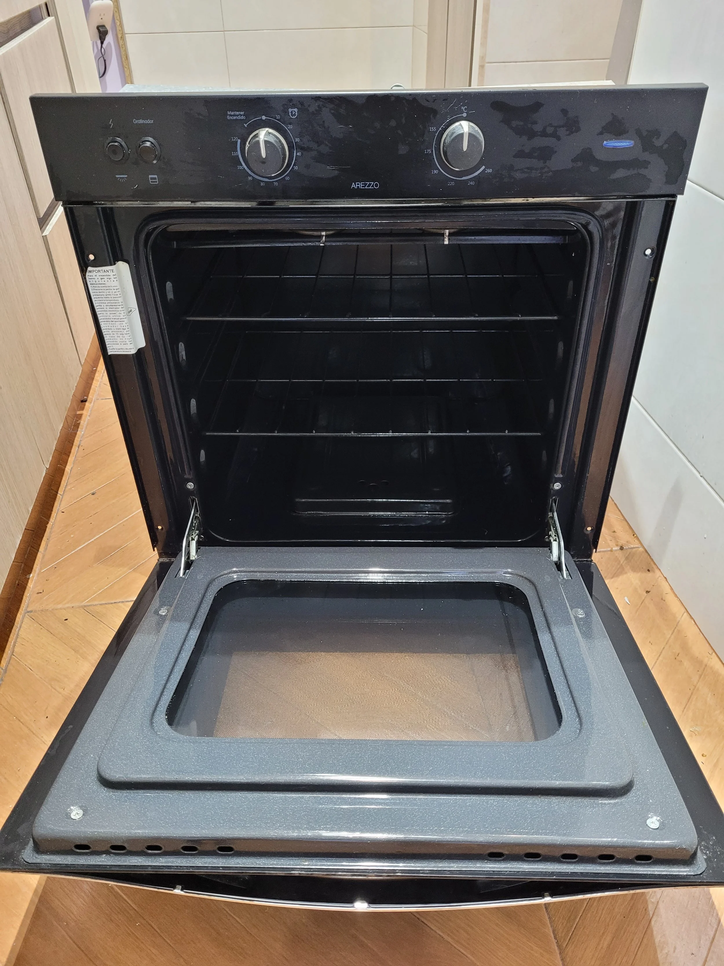 Estufa eléctrica con puerta de vidrio que está abierta, mostrando el interior con estantes y la superficie superior con knob de controles.