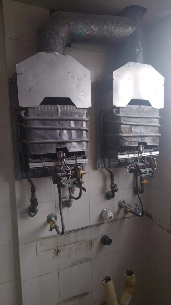 Dos calentadores de agua instalados en la pared, con tuberías de metal y conexiones eléctricas, en una habitación de servicio o lavandería.