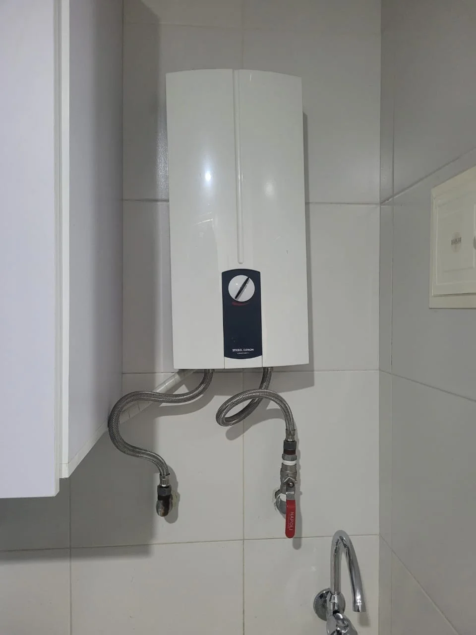 Calentador de agua eléctrico en la pared de una cocina con tubos y fuga de agua.