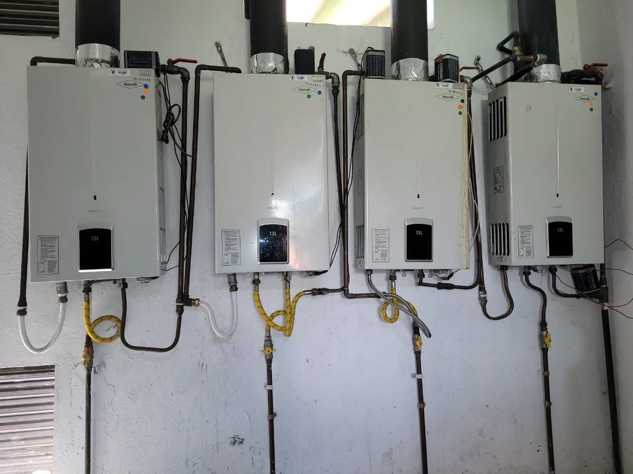 Cuatro calentadores de agua blancos instalados en una pared, con tuberías de cobre y conexiones eléctricas.
