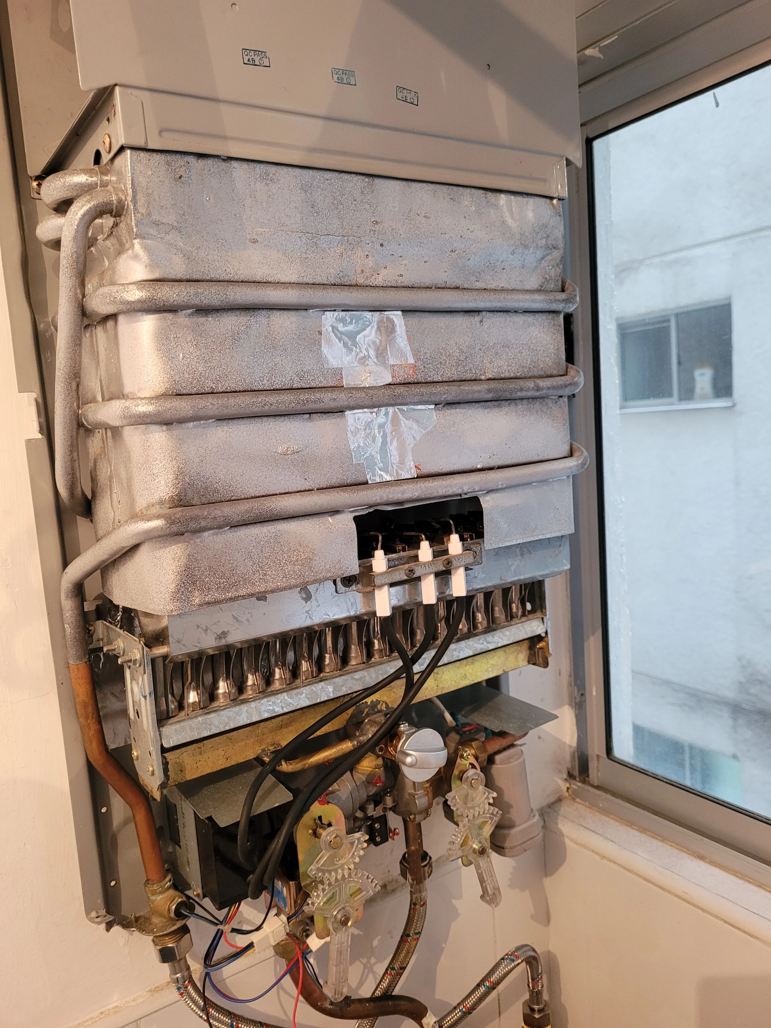 Componentes internos de una caldera de calefacción, incluyendo tuberías, válvulas y cables.